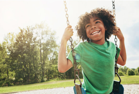 Happy, nature and child on swing in park for fun, adventure and play time on holiday or weekend trip. Smile, cute and boy kid on motion equipment on playground in outdoor field on vacation in Brazil.
