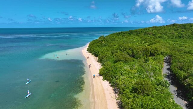Aerial drone footage over a beautiful beach near Fajardo, Puerto Rico, with people walking and paddle boarding