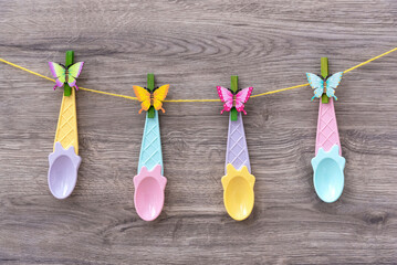 A set of colored ice cream spoons are hanging on a clothespin. Decorative plastic spoons. Beige...