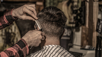 Close up of a professional barber working giving a haircut to a man. Hipster client getting...