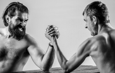 Heavily muscled bearded man arm wrestling a puny weak man. Two man's hands clasped arm wrestling,...