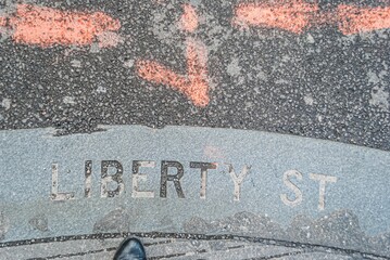 A person's shadow is cast on the ground in front of a Liberty Street sign