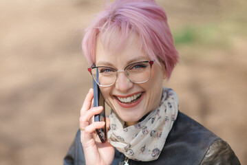 close-up portrait of young caucasian woman with coloured pink hair in park smiling widely and...