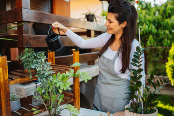 One young caucasian woman is taking care of her plants using plant mister and water can	