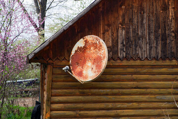 Image of an old TV satellite parabolic antenna attached to the wall of a wooden house