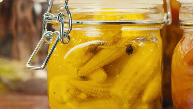 Close-up of fermented yellow mini corn with black pepper in can. Preservation of vegetables in glass jars. Fermentation preserved mini corns with spices.