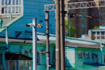 Two opposing surveillance cameras on a metal pole against building backdrop