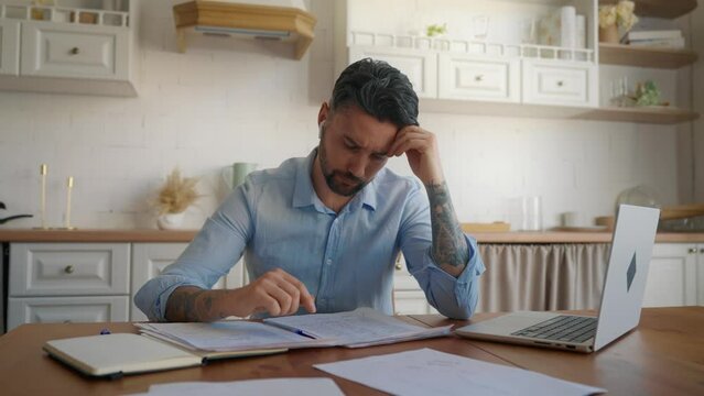Depressed desperate man doing paperwork. Stressed tired handsome businessman working with laptop at home looking at paying bills in finance, looking frustrated. Money debt, budget, stress concept.