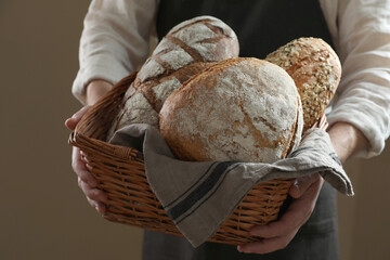 Man holding wicker basket with different types of bread on brown background, closeup