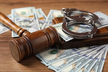Judge's gavel, money and handcuffs on wooden table, closeup