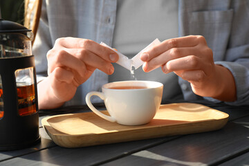 Woman adding sugar into cup of tea at black wooden table, closeup