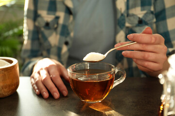 Woman adding sugar into cup of tea at dark table, closeup