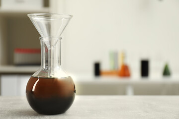 Flask with brown crude oil and filter funnel on light grey table, space for text