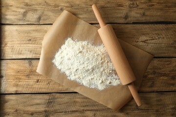 Parchment with flour and rolling pin on wooden table, top view