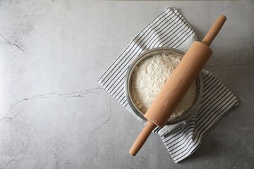 Flour in bowl, rolling pin and napkin on grey table, top view. Space for text