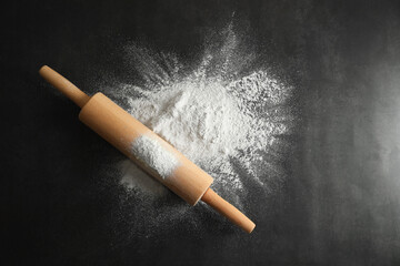 Scattered flour and rolling pin on black table, top view. Space for text