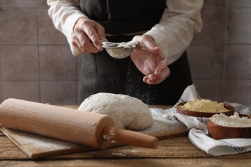 Woman sprinkling flour over dough at wooden table, closeup