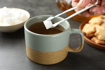 Woman adding sugar cube into aromatic tea at grey table, closeup