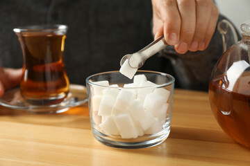Woman adding sugar cube into aromatic tea at wooden table, closeup