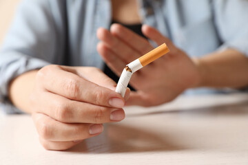 Stop smoking. Woman holding broken cigarette at table, closeup