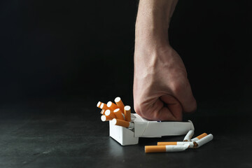 Stop smoking. Man crushing pack with cigarettes on dark background, closeup. Space for text