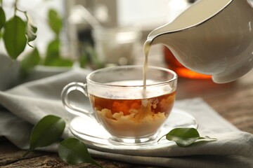 Pouring milk into cup with tea on wooden table, closeup