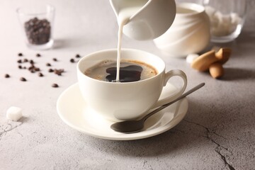 Pouring milk into cup with coffee on light grey textured table, closeup