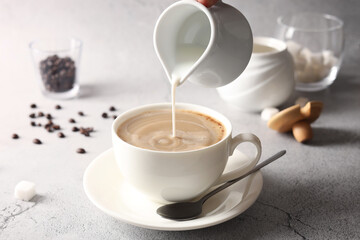 Pouring milk into cup with coffee on light grey textured table, closeup