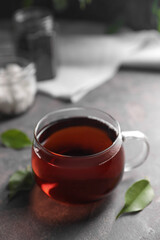 Tasty hot tea in cup and leaves on grey table, closeup