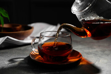 Pouring hot tea into cup on grey table, closeup