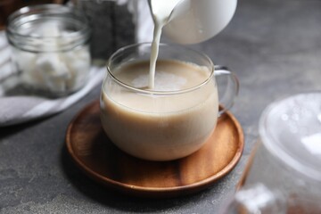 Pouring milk into cup of tea on grey table, closeup