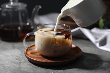Pouring milk into cup of tea on grey table, closeup