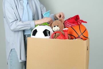 Woman with box of unwanted stuff on grey background, closeup