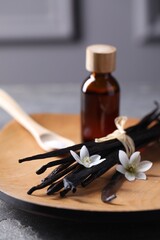 Vanilla pods, flowers and bottle of essential oil on grey table, closeup