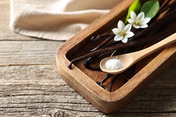 Vanilla pods, flowers, leaves and spoon with sugar on wooden table, closeup. Space for text
