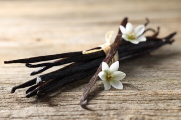 Bunch of vanilla pods and flowers on wooden table, closeup
