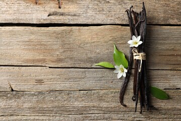 Bunch of vanilla pods, flowers and leaves on wooden table, top view. Space for text