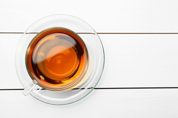 Glass cup of tea on white wooden table, top view. Space for text