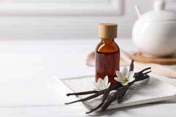 Vanilla pods, essential oil and flowers on white wooden table, space for text