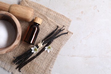 Vanilla pods, essential oil, flowers and sugar in bowl on light gray table, flat lay. Space for text
