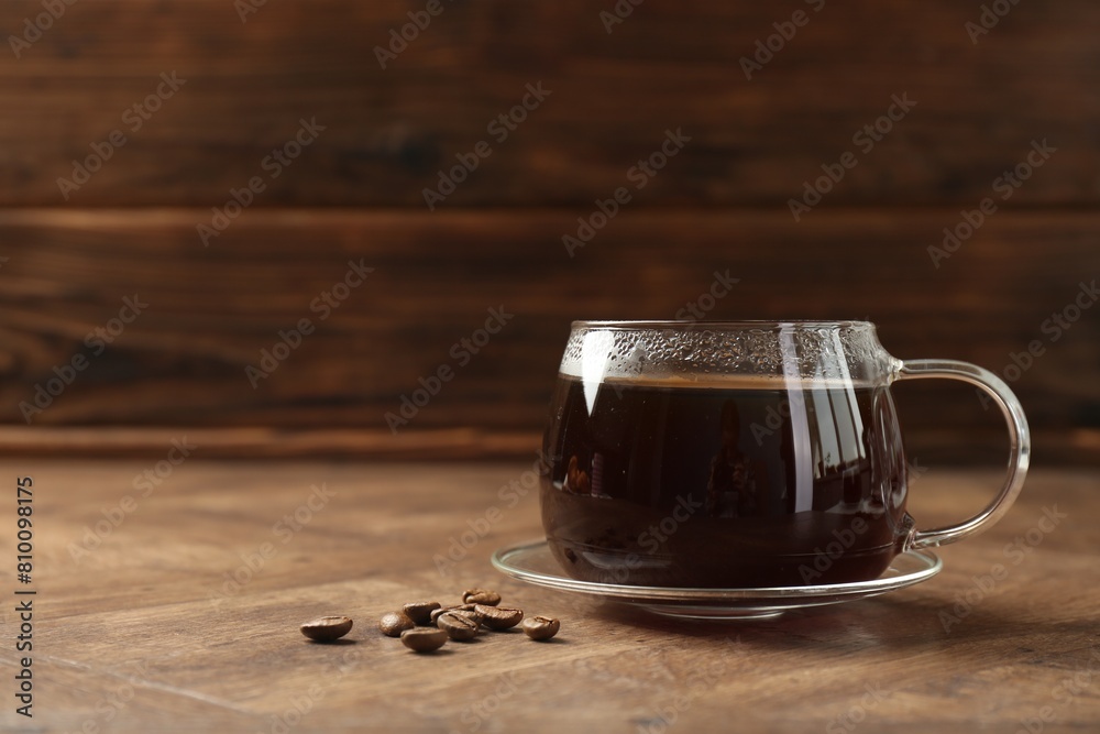 Canvas Prints Hot coffee in glass cup and beans on wooden table, closeup. Space for text