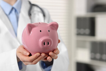 Doctor with pink piggy bank indoors, closeup. Space for text