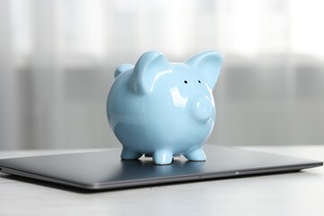 Piggy bank and laptop on white table indoors