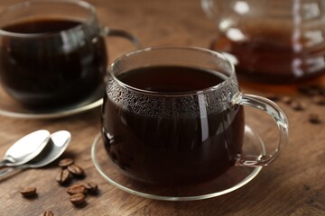 Hot coffee in glass cups, spoons and beans on wooden table, closeup