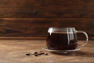 Hot coffee in glass cup and beans on wooden table, closeup. Space for text