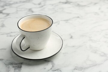 Tasty cappuccino in cup and saucer on white marble table, closeup. Space for text