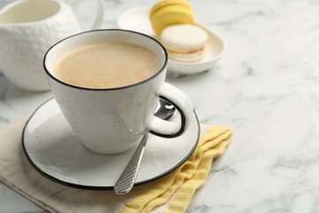 Tasty cappuccino in cup, spoon and saucer on white marble table, closeup. Space for text