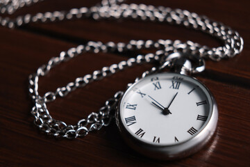 Silver pocket clock with chain on wooden table, closeup