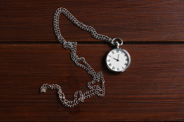 Silver pocket clock with chain on wooden table, top view