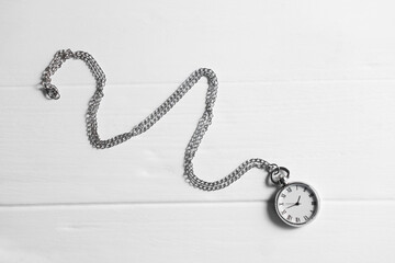 Silver pocket clock with chain on white wooden table, top view